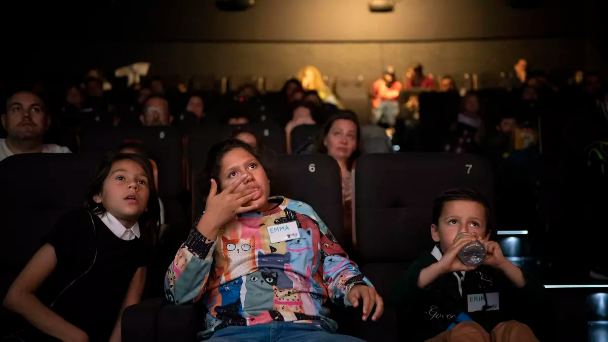 Tres niños disfrutan de una sesión de cine adaptada organizada por Ventea en los Cines Embajadores de Madrid.